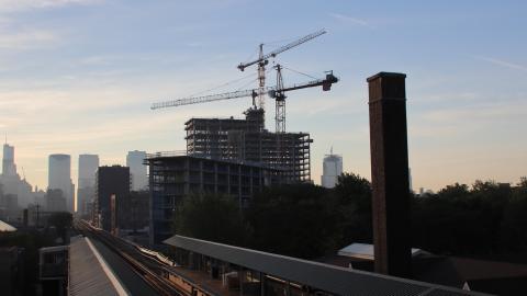 Two construction cranes tower above an apartment development with a line of tall buildings in the background. 